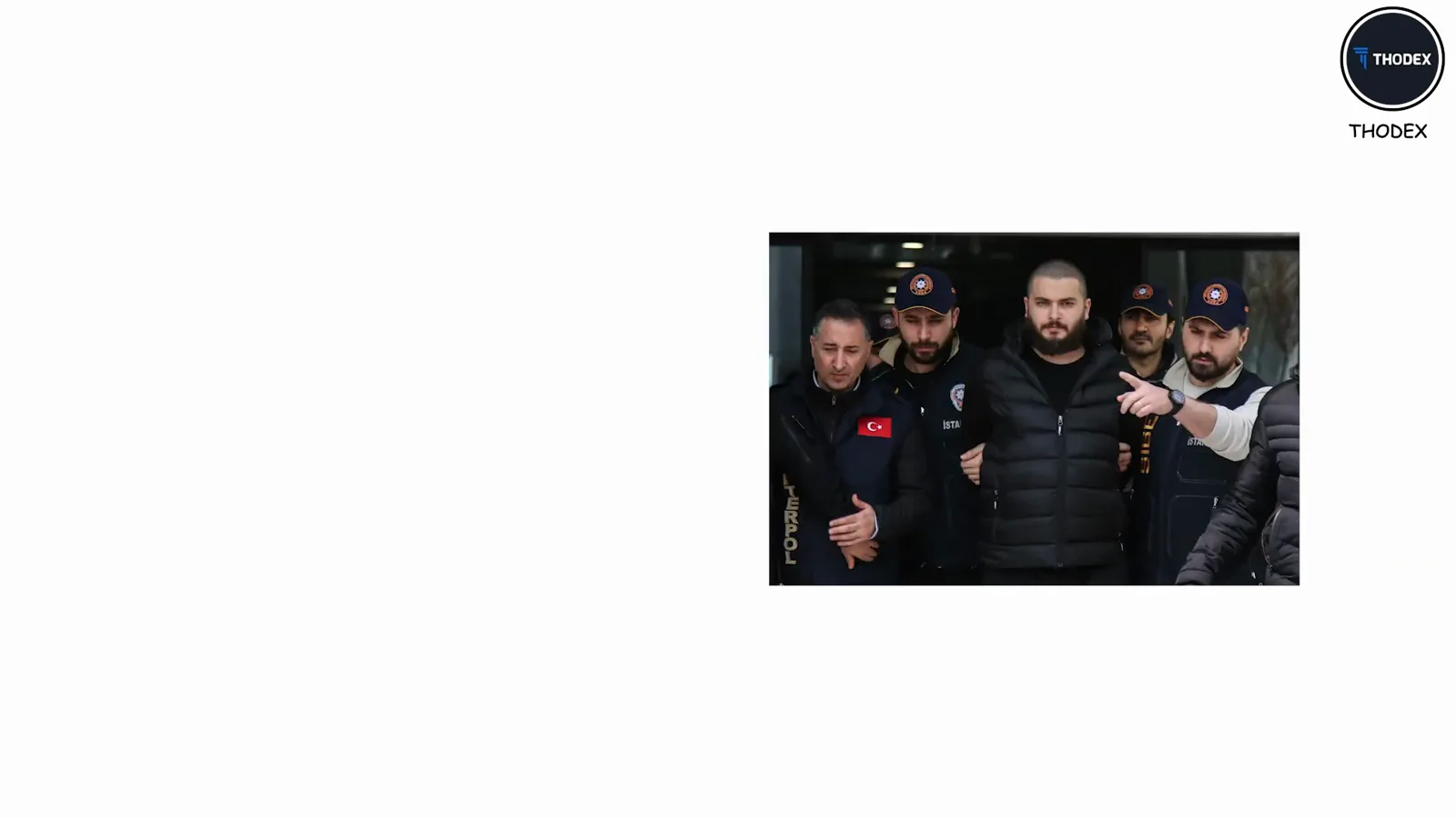 Thodex founder Faruk Özer in a black puffer jacket flanked by Turkish police officers after his capture in Albania