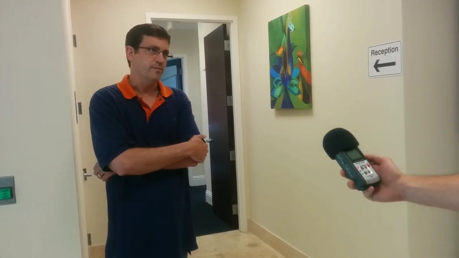 Still from the August 2014 office visit showing a South Florida Bitcoin meetup organizer being handed a microphone beside the reception sign at Cryptsy headquarters