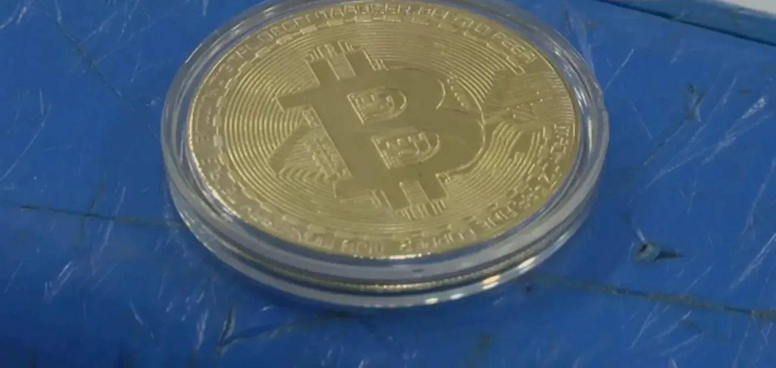Commemorative gold bitcoin coin in a clear case resting on a blue tarp, the symbol of El Salvador's 2021 announcement that bitcoin would become legal tender Commemorative gold bitcoin coin in a clear case resting on a blue tarp, the symbol of El Salvador's 2021 announcement that bitcoin would become legal tender